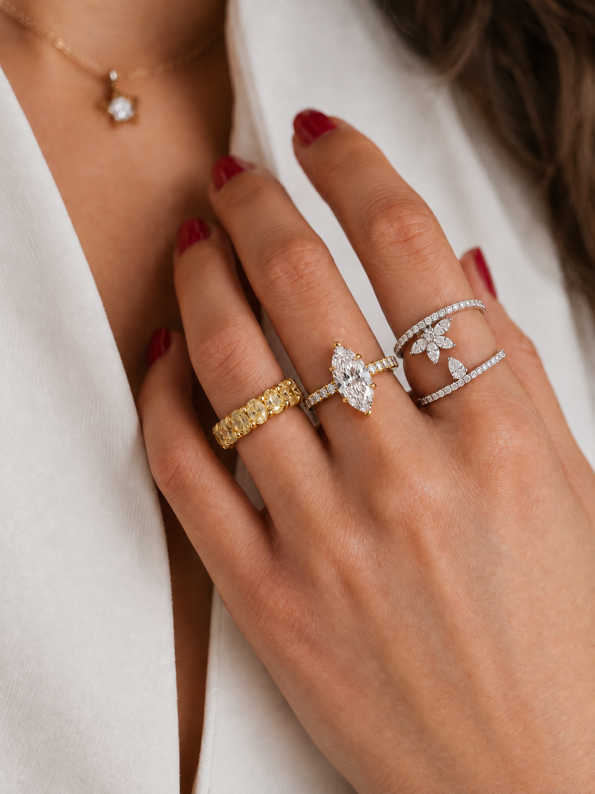 A close-up of a woman's hand wearing multiple fine jewelry rings, including a yellow gold band, a silver marquise-shaped ring with a clear gemstone, and a silver double-band with pavé stones 18K gold diamonds from The Private Room Fine Jewelry
