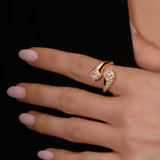 A close-up of a hand wearing a rose gold wrap ring with pavé-set clear stones, set against a solid black background.