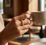 **A RADIANT LEGACY CAPTURED IN GOLD** — ring lifestyle shot, Close-up of a hand holding a coffee cup, ring visible on finger